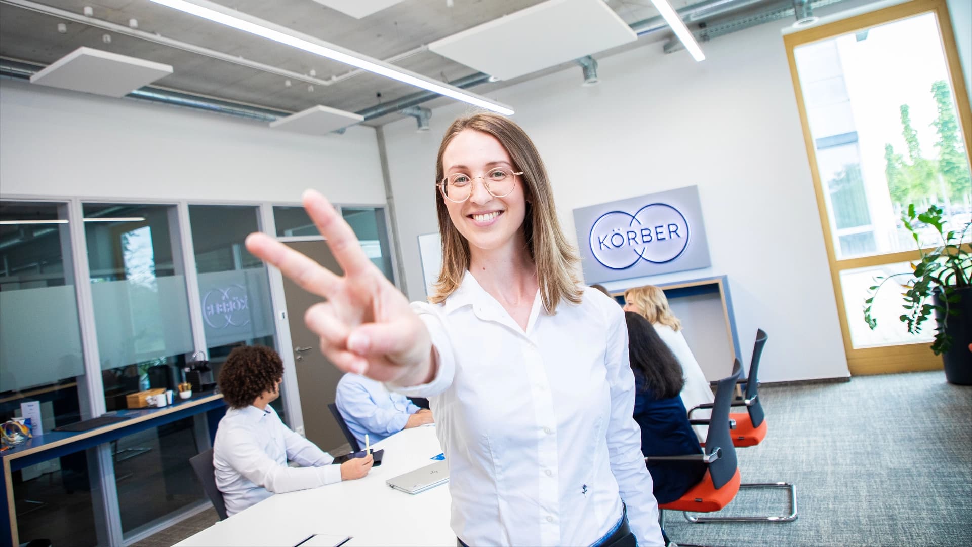 A woman in a business meeting room has her hands up, contributing to the conversation with her colleagues.
