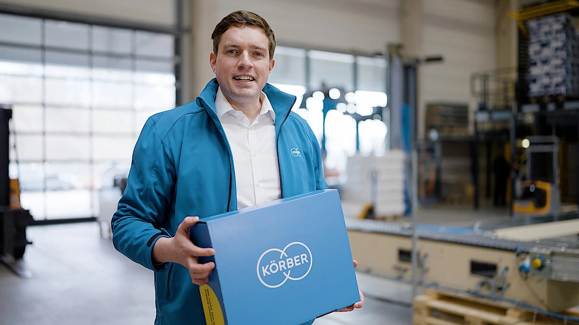 Körber employee holding a blue package with the Körber logo.