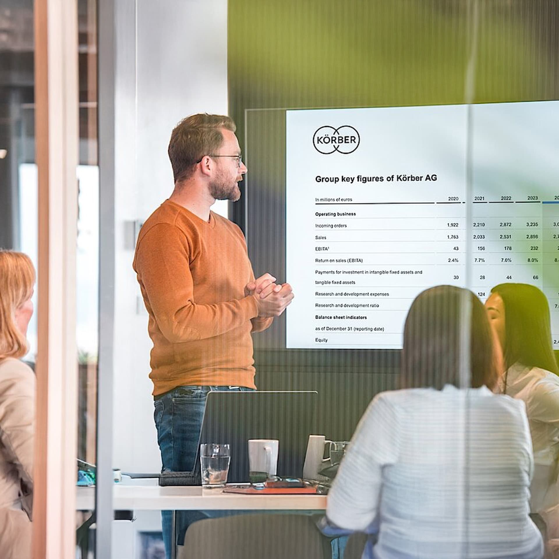 Man presenting Körber's key financial figures in a meeting room with other team members