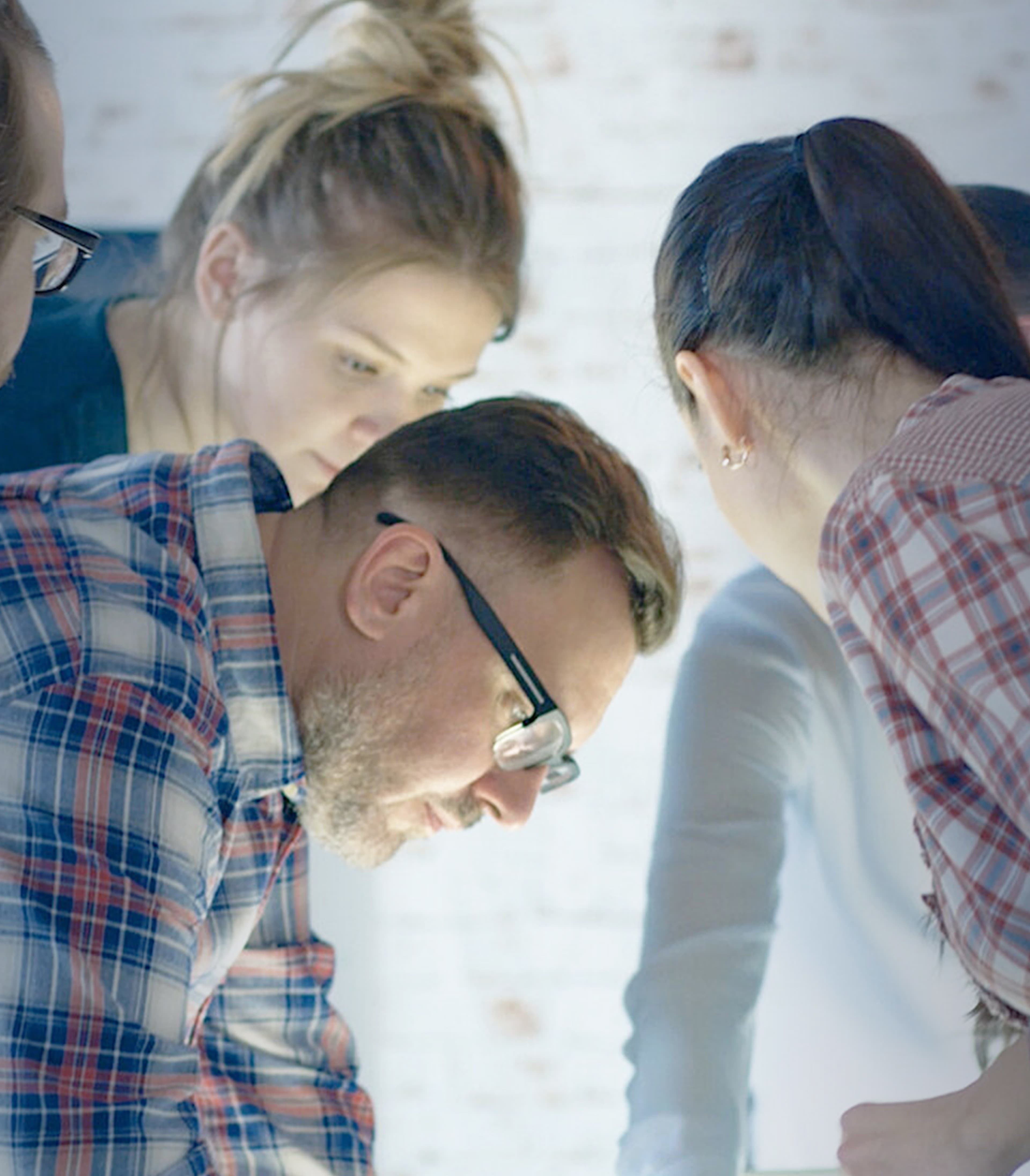 Group of people working together looking down over a table that is out of shot