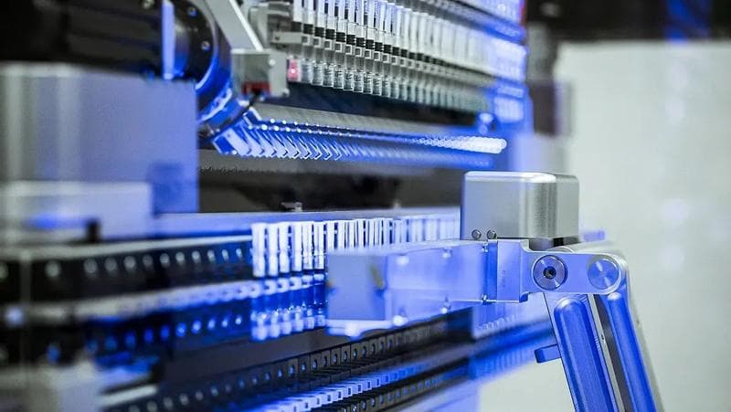 Close-up of a machine with blue lights, part of Körber Pharma's automated syringe handling system.