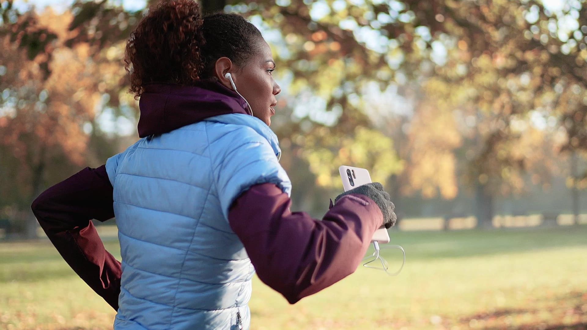 A woman with headphones running in a park, surrounded by trees and open space, engaged in her workout.