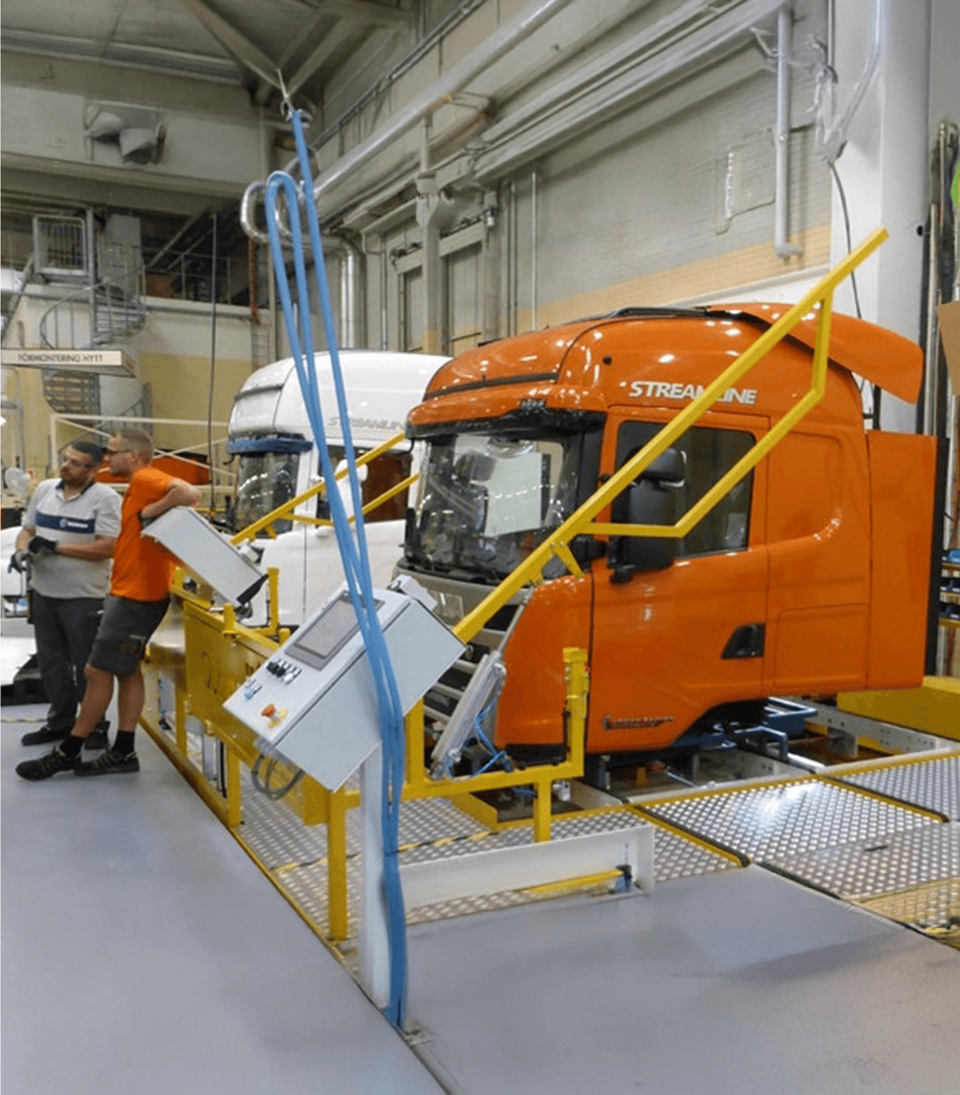 Two men standing next to a Scania assembly line