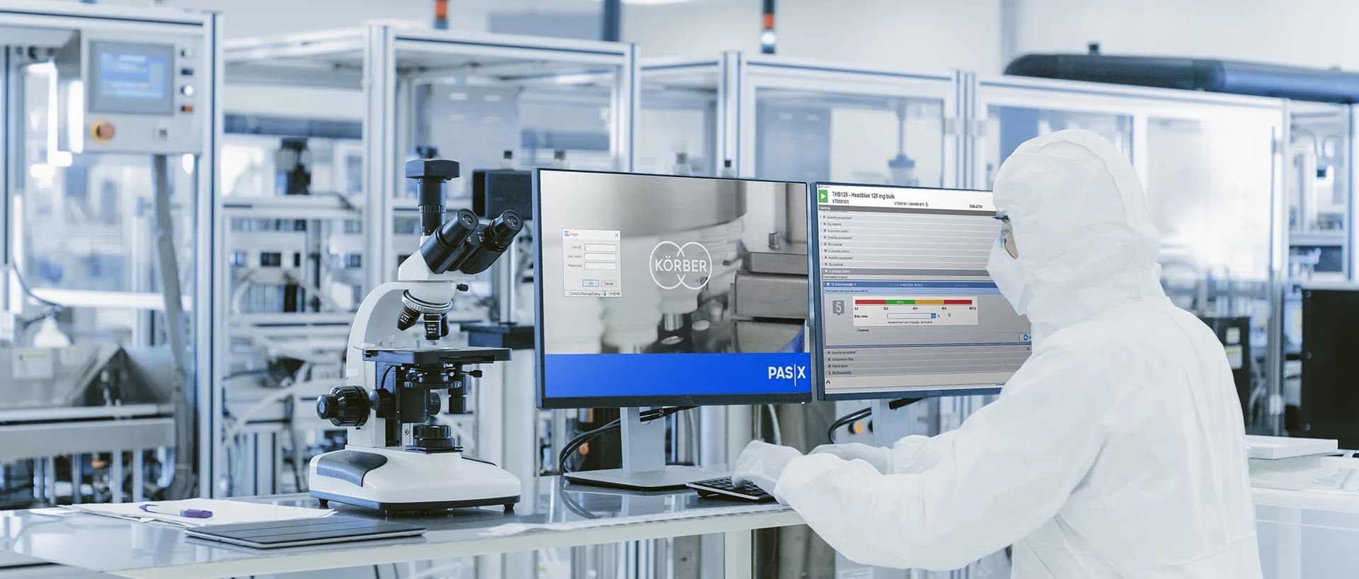 A person in a white lab coat working on a computer, focused on the Korber Pharma PAS-X MES system.