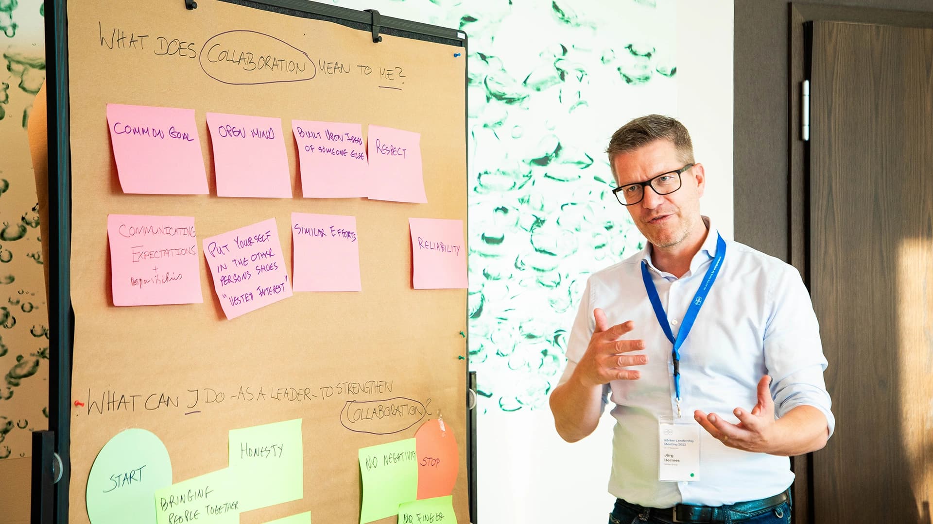 A man stands in front of a board covered with colorful sticky notes, engaged in discussion or brainstorming.