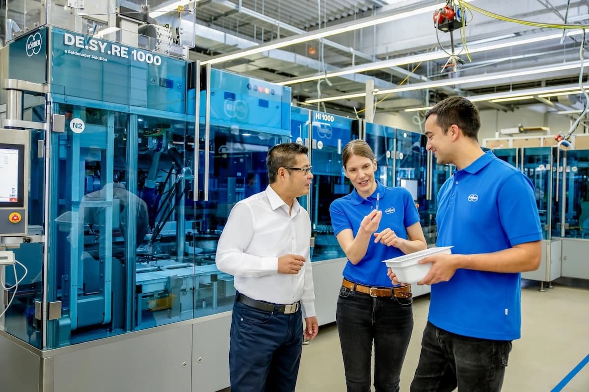 Three Körber employees engaged in conversation inside a Körber Pharma packaging factory.