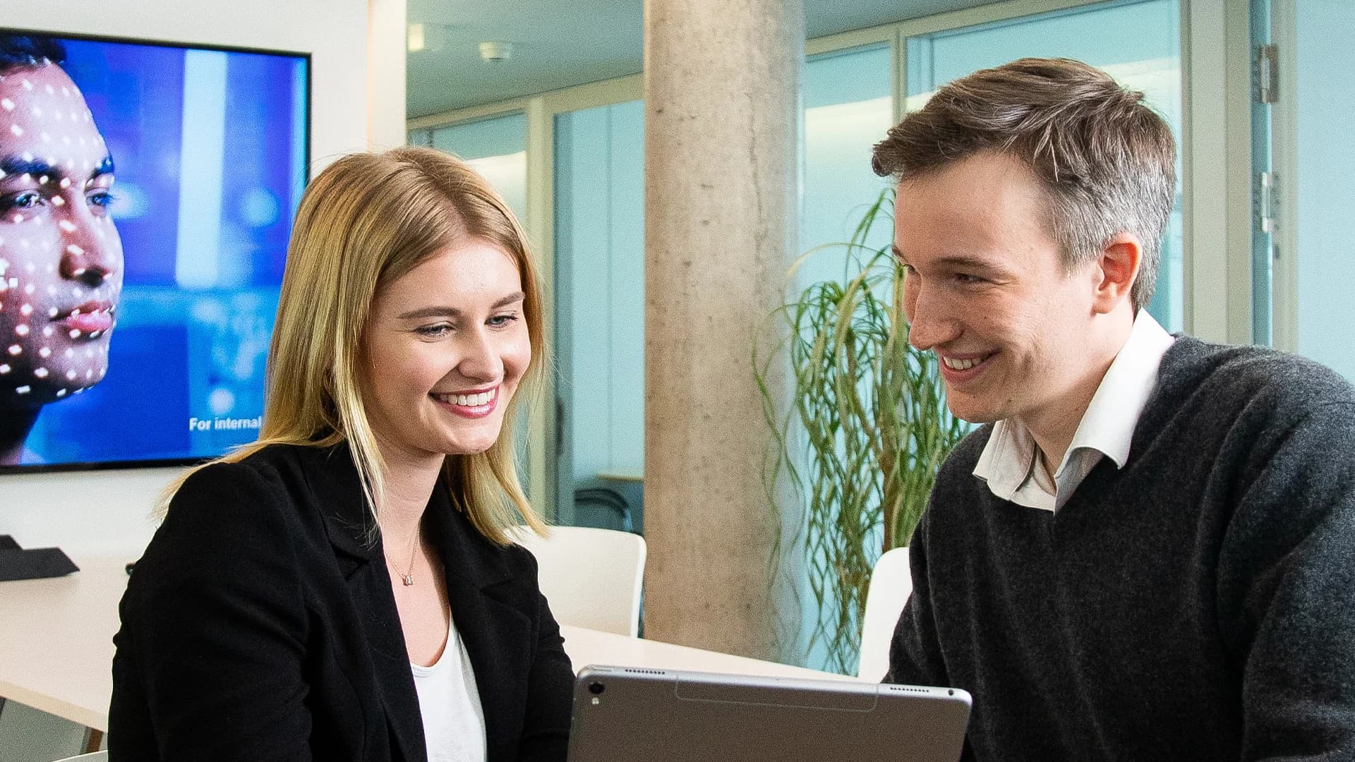 A man and woman are seated at a table using a laptop