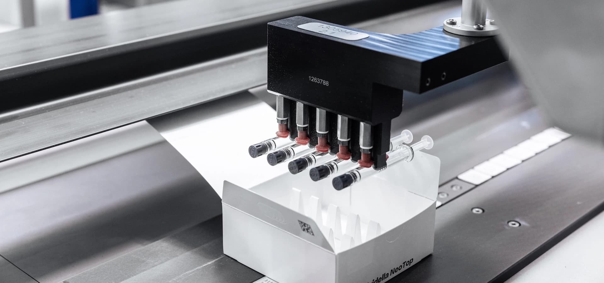 A machine works on a second machine, which is holding a box, part of the Dividella Neo Top pharma packaging process.