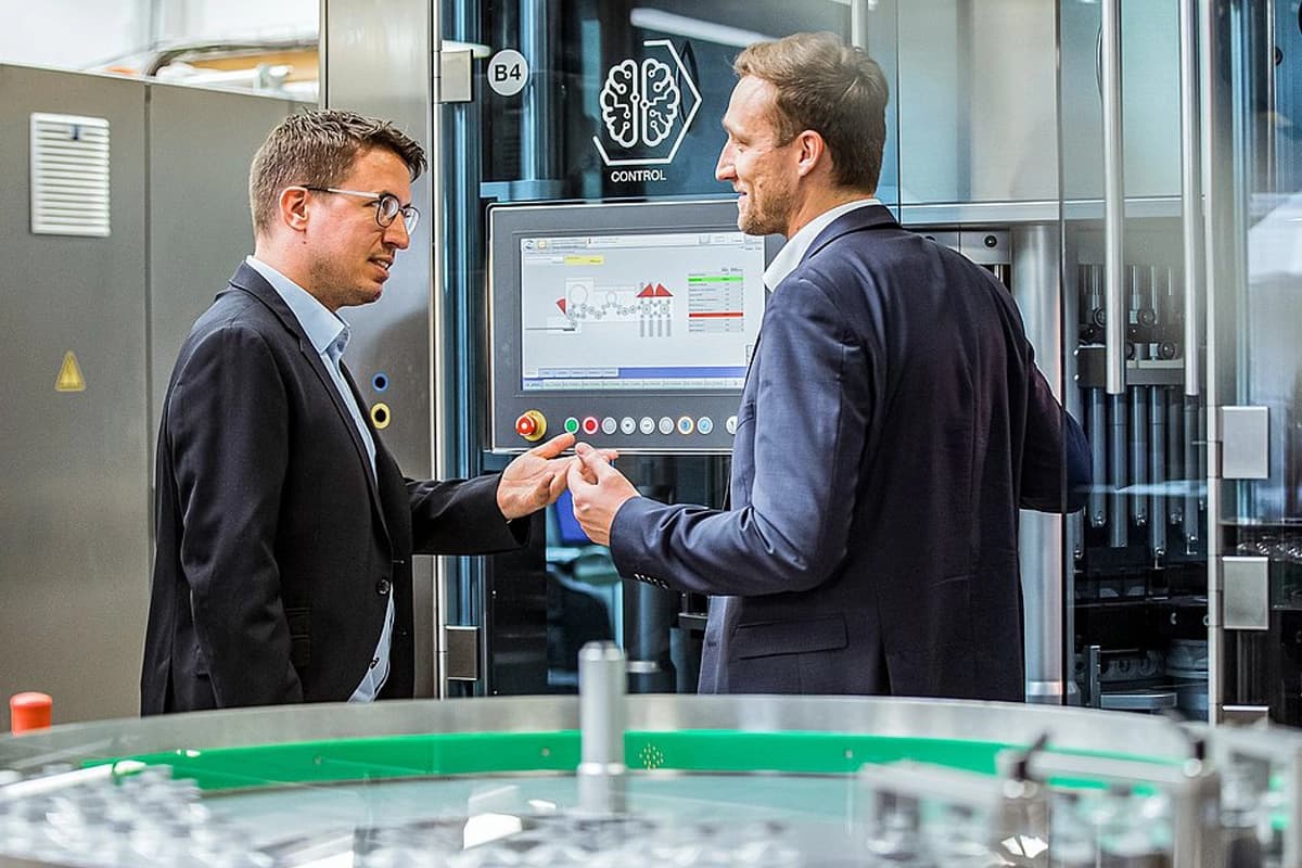 Two man in suits speaking to each other in a factory setting. 