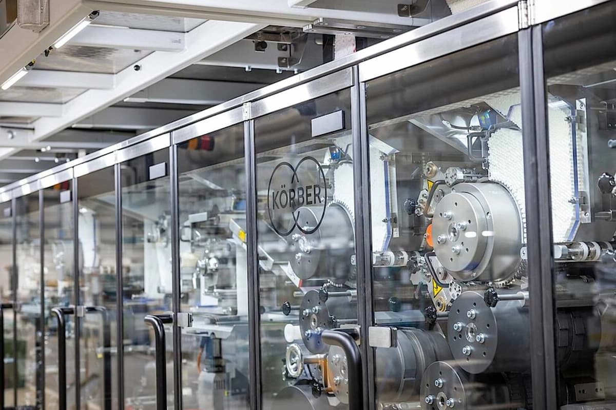 Photo of a window with the Körber logo. Behind the window is a Multi Segment Maker machine.