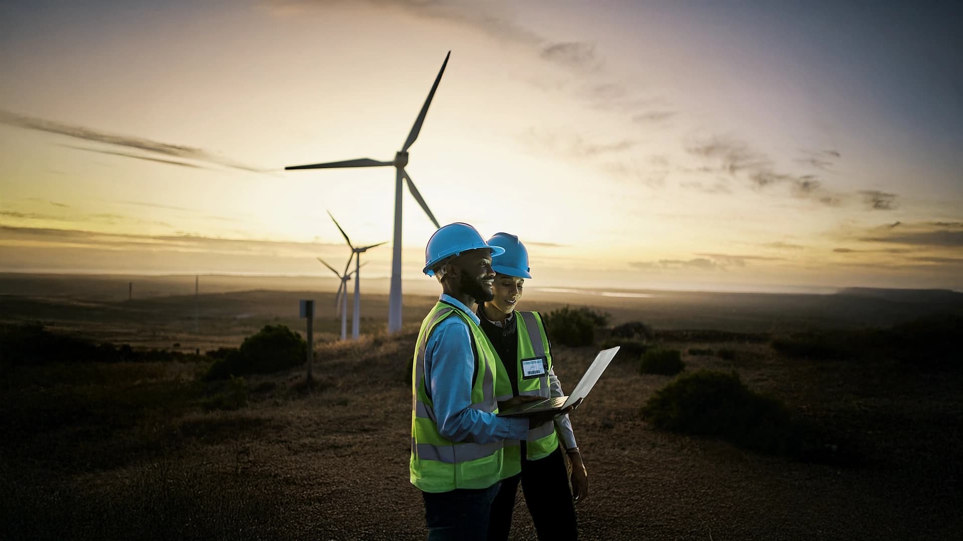 Two environmental workers in a field with wind turbines