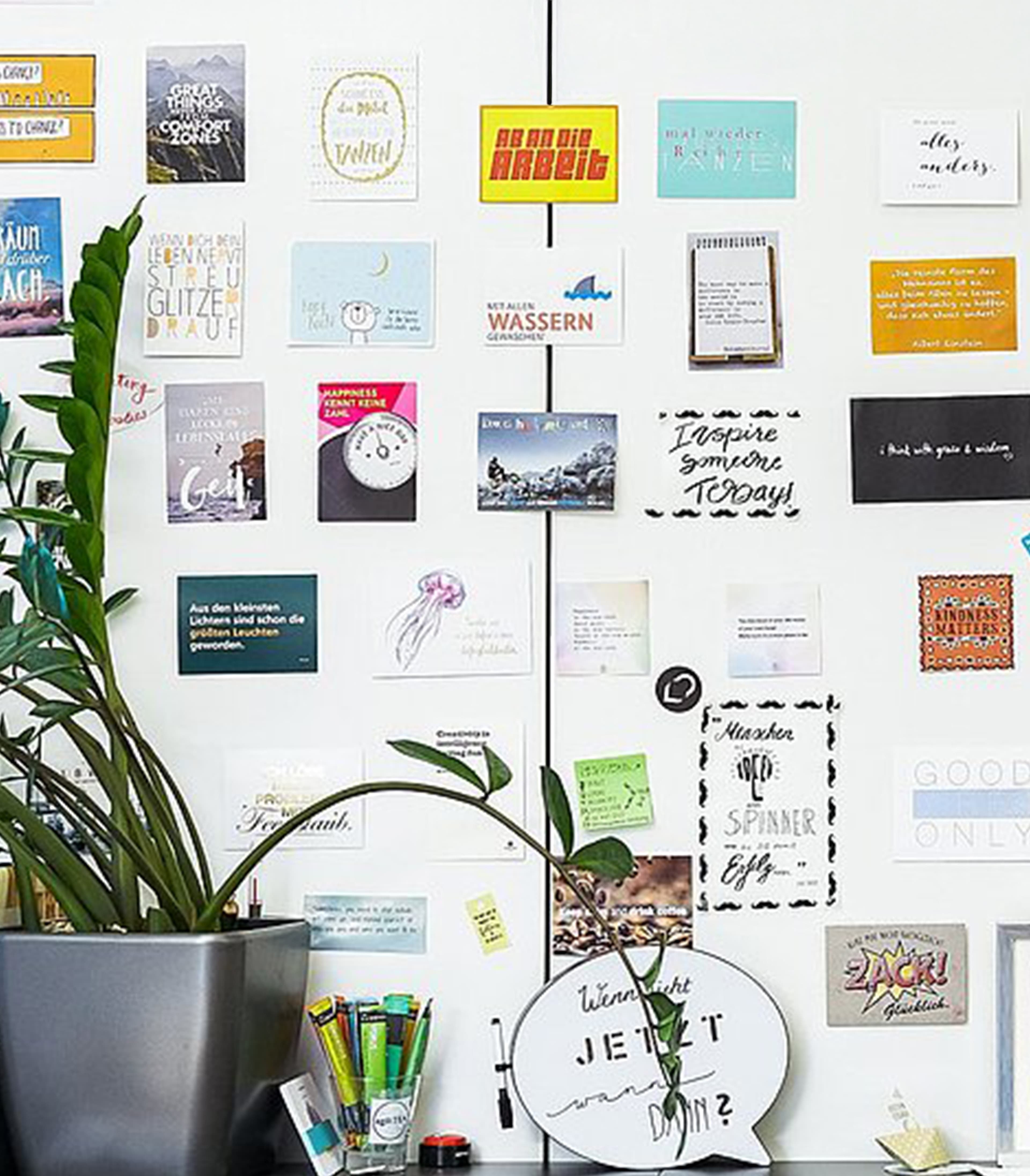 Wall covered in postcards and a plant on a shelf