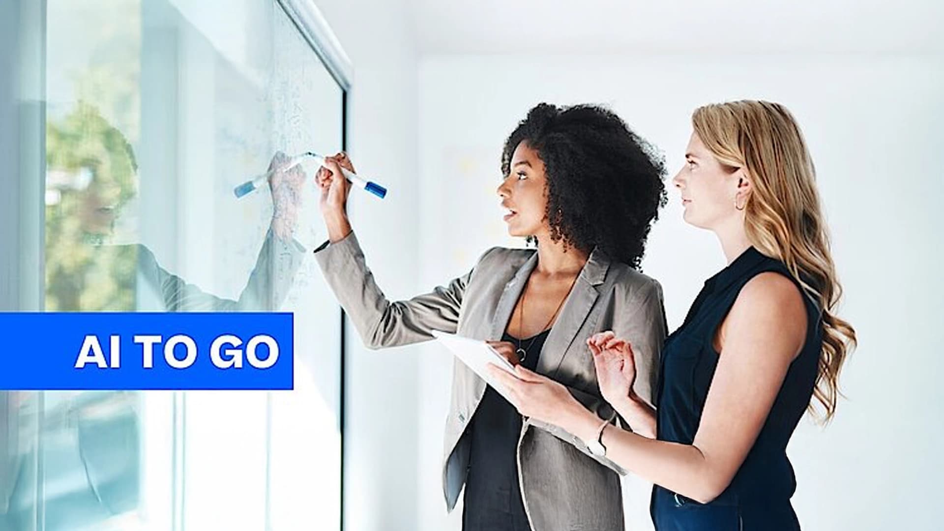 Two woman in an office setting talking writing in a white board, talking about AI in marketing