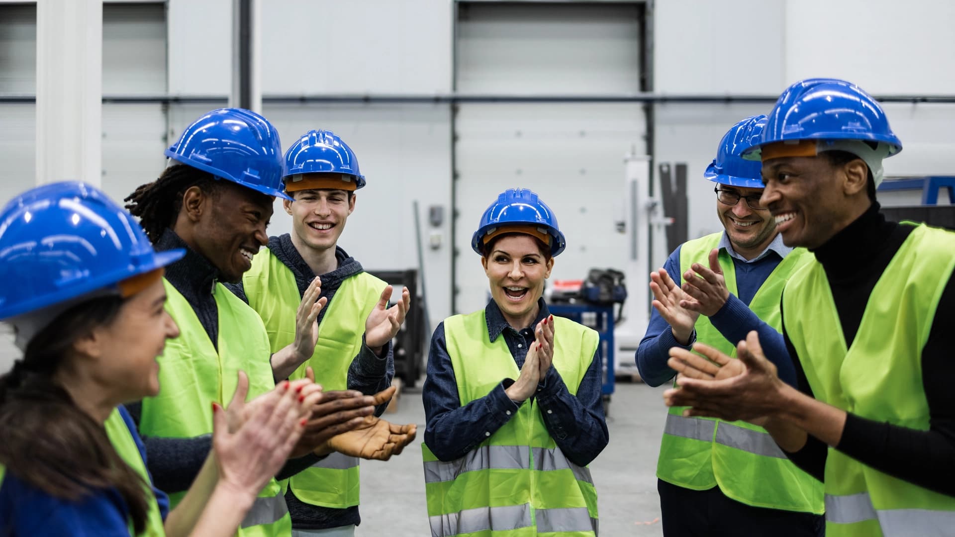 A group of factory workers clapping together, celebrating a successful achievement or milestone in their workplace.