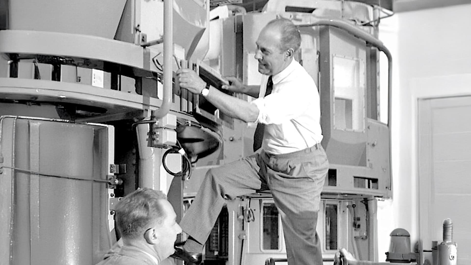Black and white photo of two men next to a machine