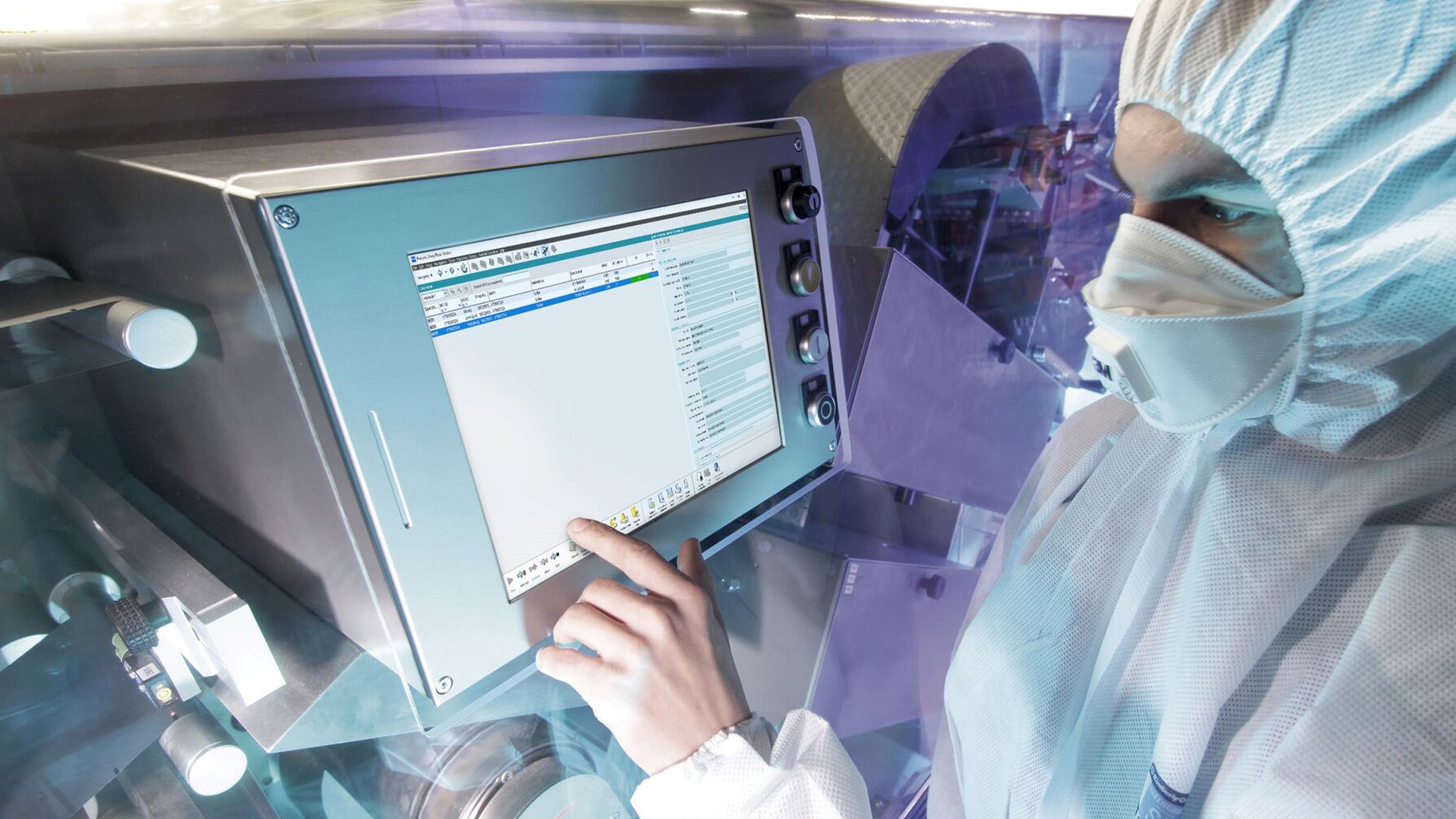 Person wearing personal protective equipment using pharma software on a touchscreen.