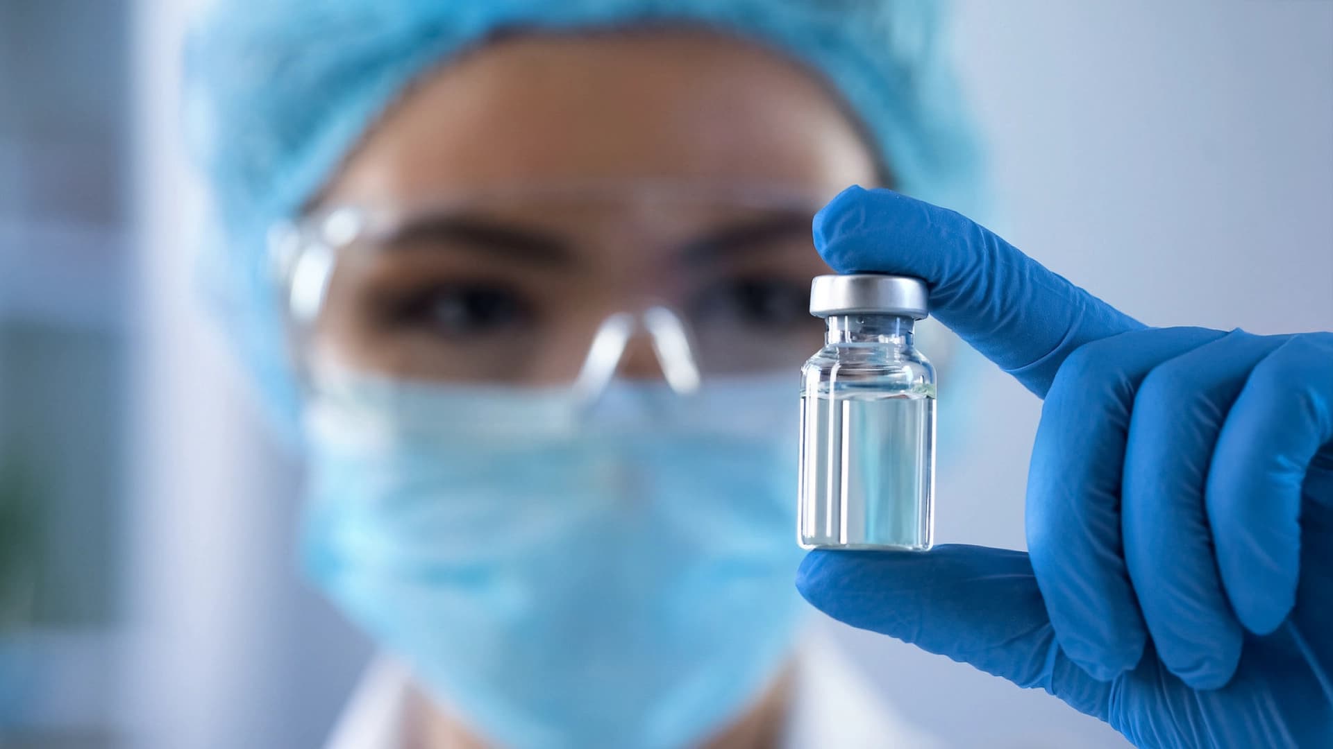 Körber employee with chemical safety glasses and a small pharma flask with medicine inside.