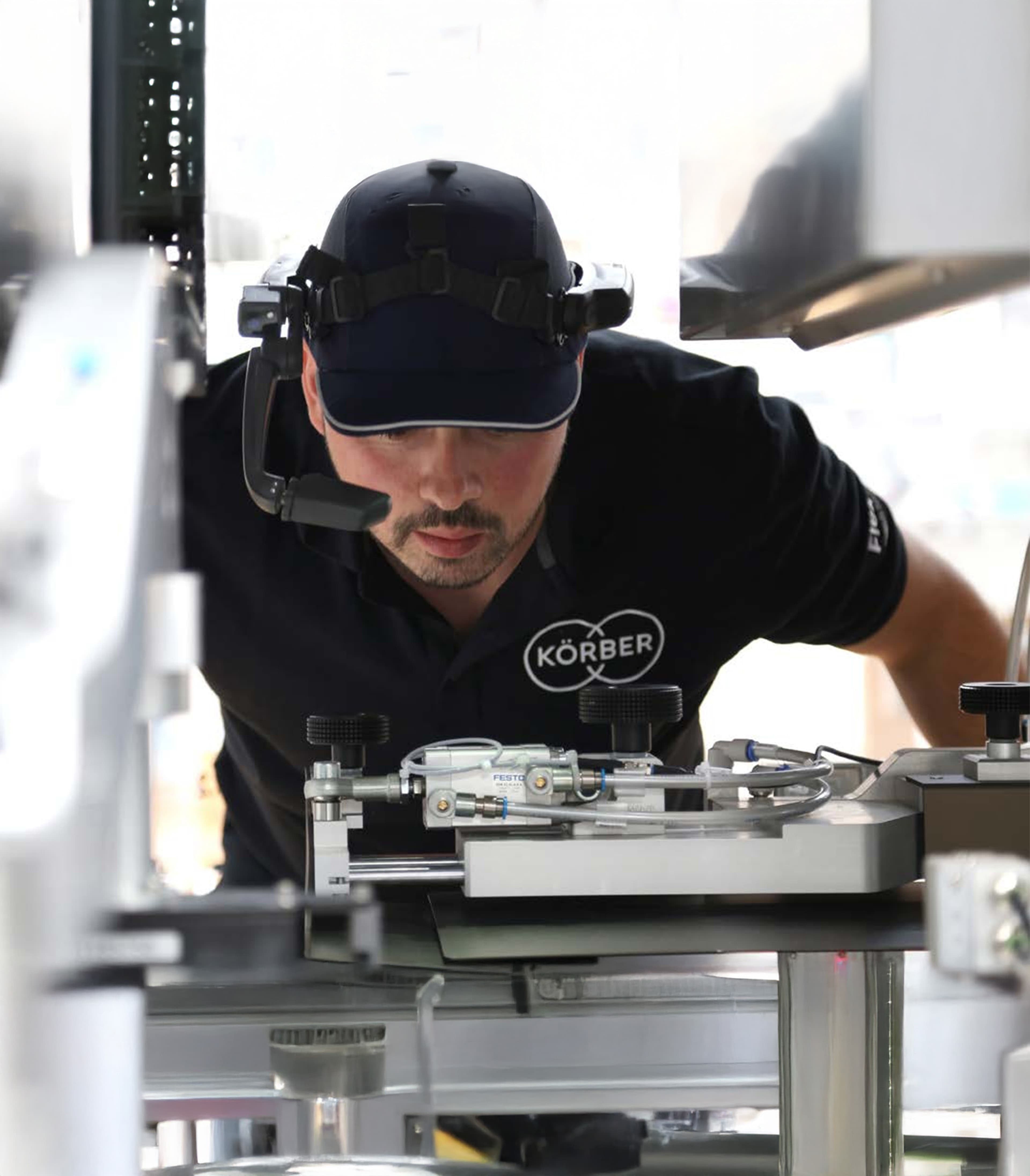 A technician with a headset and cap inspects industrial machinery at Körber.