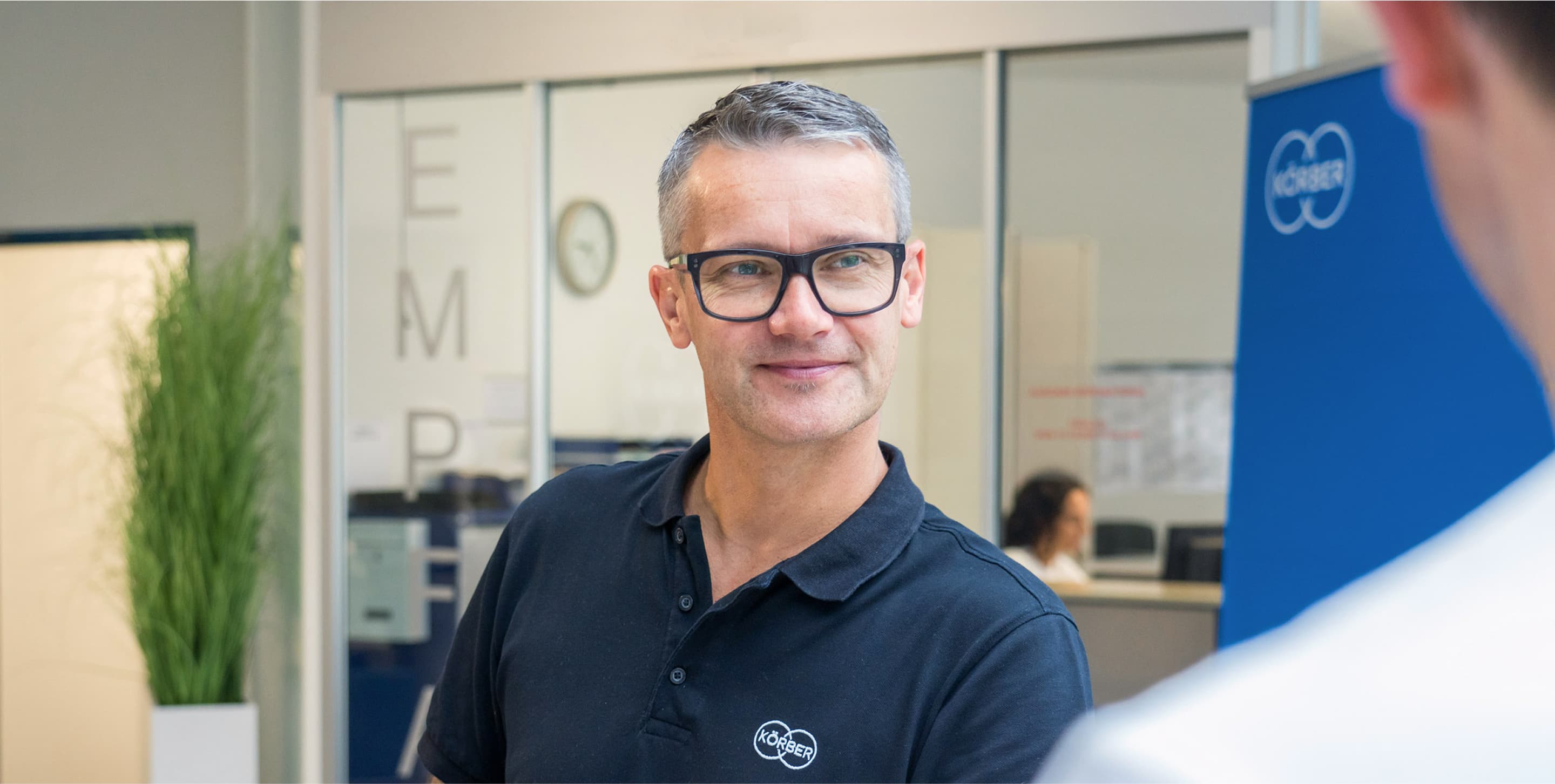 Man wearing black glasses and a black Körber t-shirt smiling