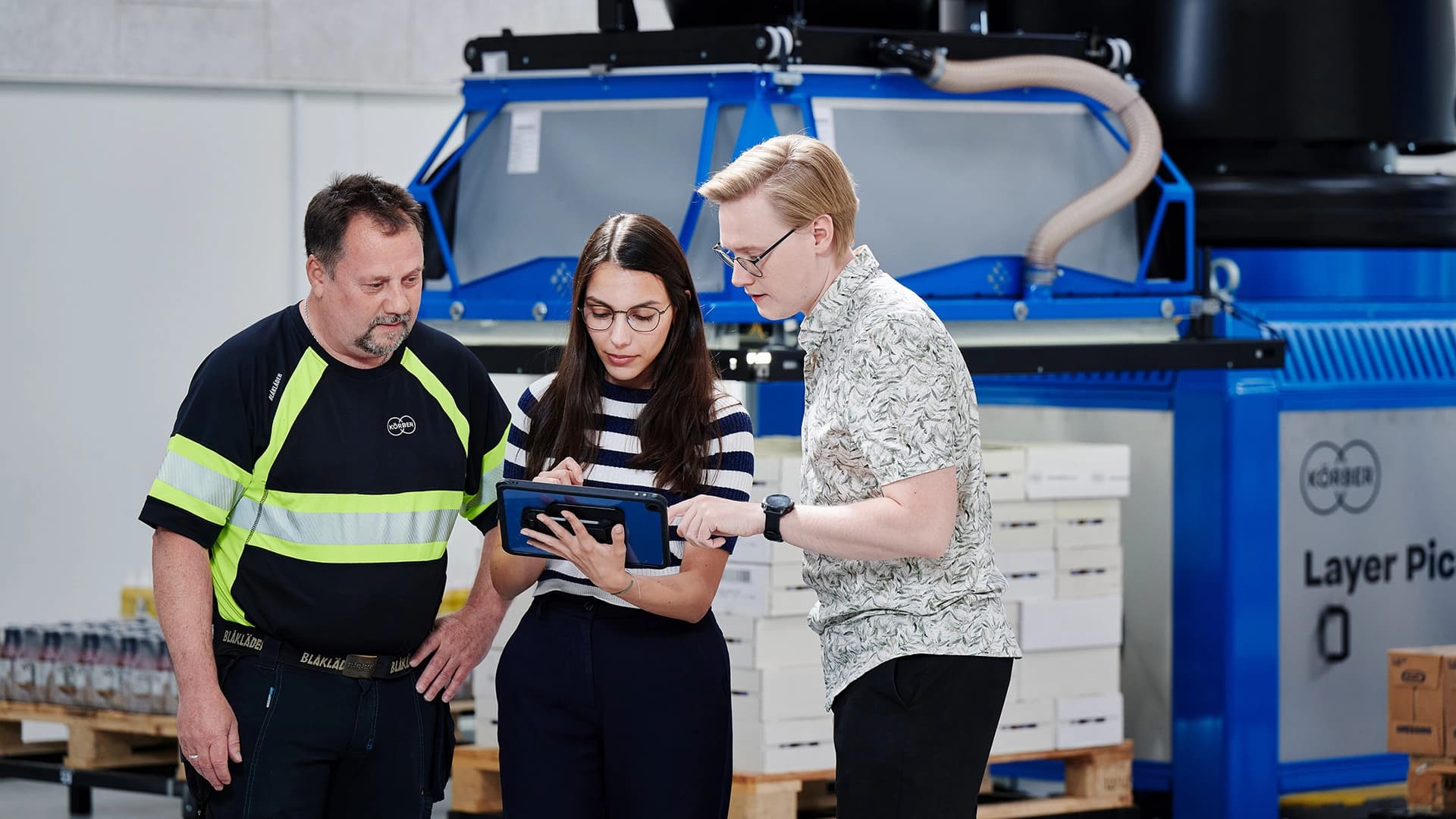 Three people examining a machine related to Körber's warehouse management system.