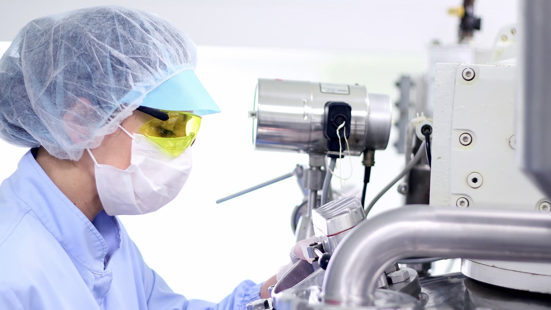Person wearing personal protective equipment looking down a microscope 