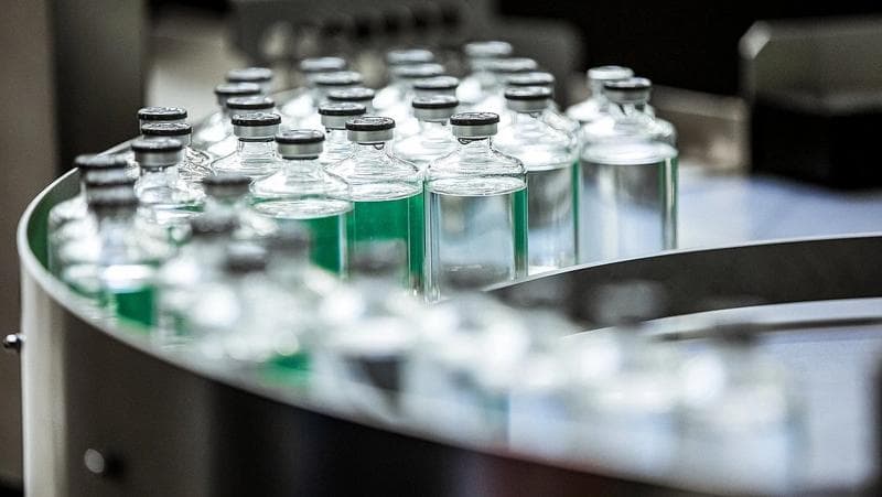 A row of bottles filled with green liquid, showcasing Körber Pharma's inspection machines for production safety.