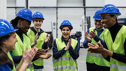 A group of factory workers clapping together, celebrating a successful achievement or milestone in their workplace