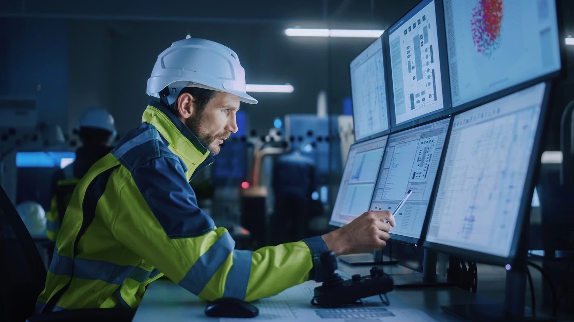 A Körber worker wearing a hardhat is focused on working on a computer at a warehouse site.