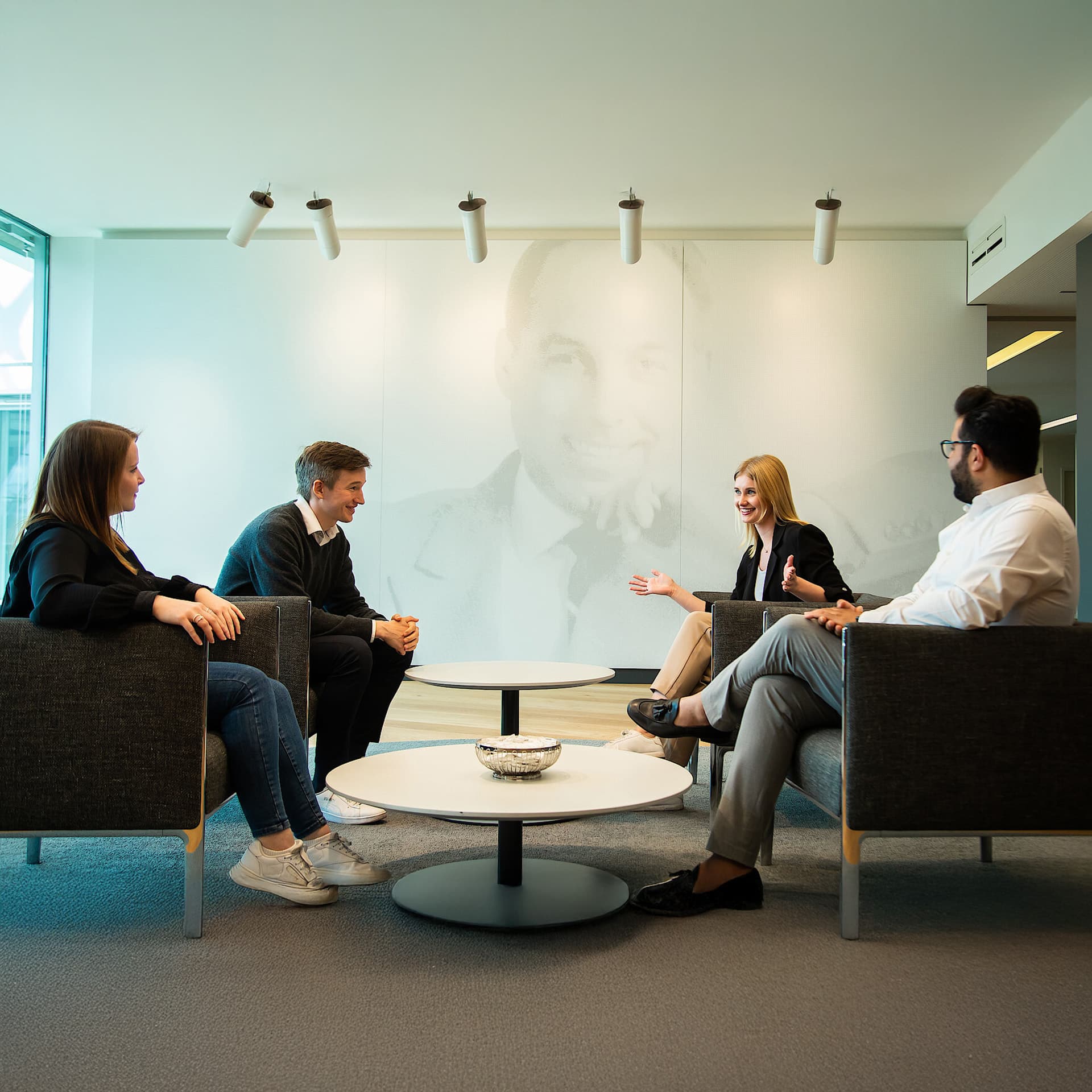 Four people sitting on armchairs in an office breakout space
