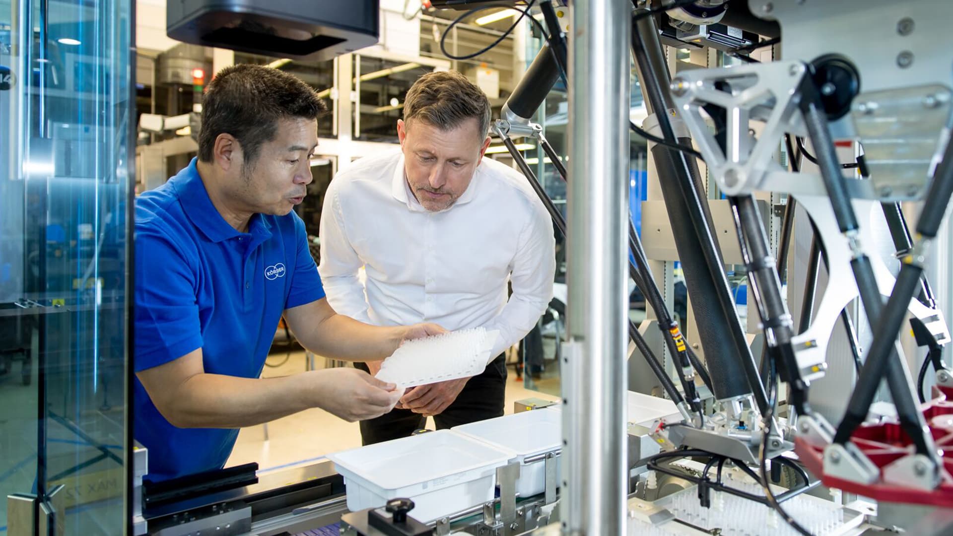 Körber employee wearing a blue t-shirt showing a man how to use a pharma machine