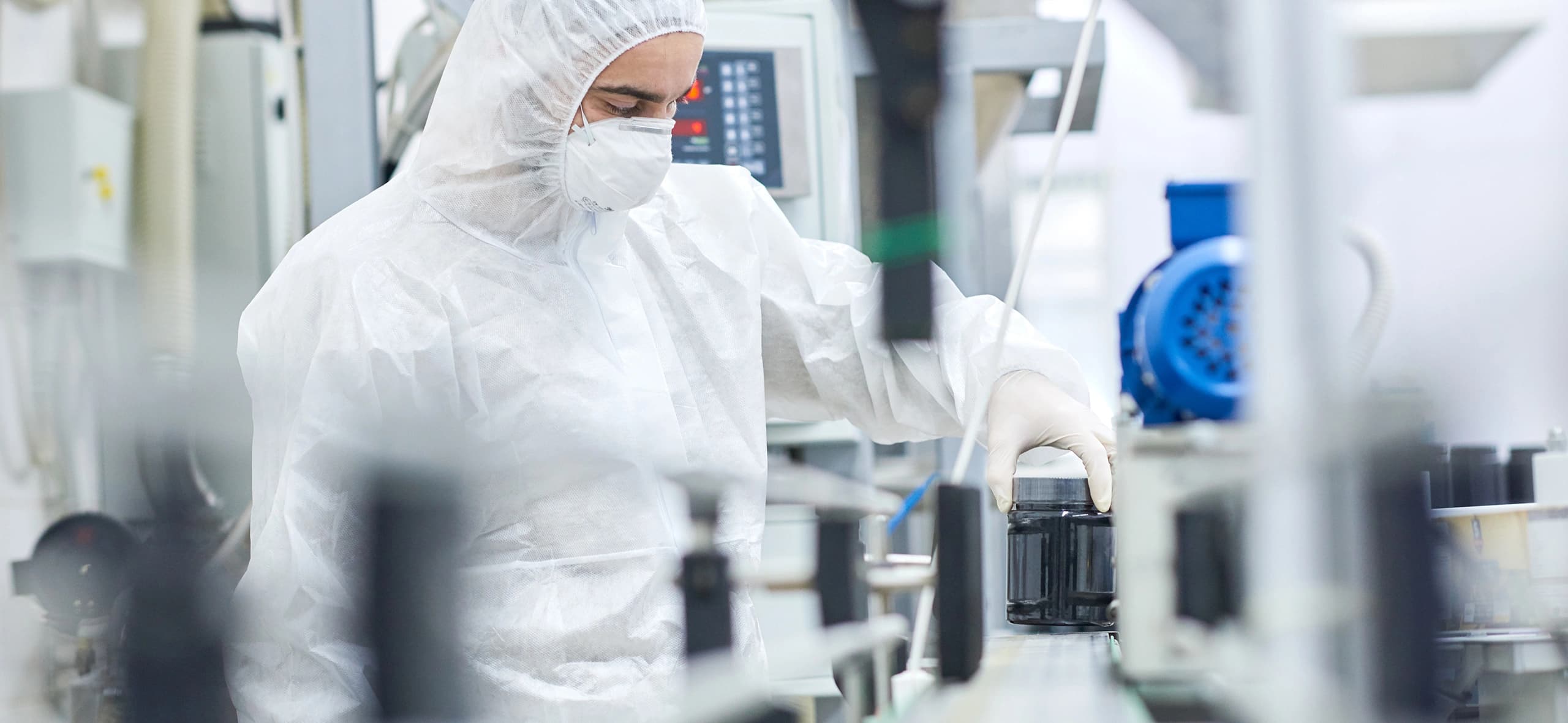 A worker in a white protective suit operates a machine in a controlled environment.
