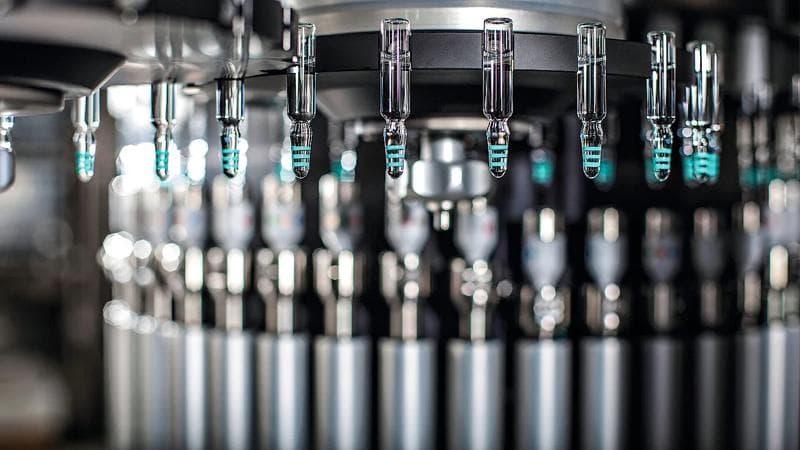 Close-up of automated pharmaceutical equipment handling vials, showcasing precision and innovation in manufacturing.