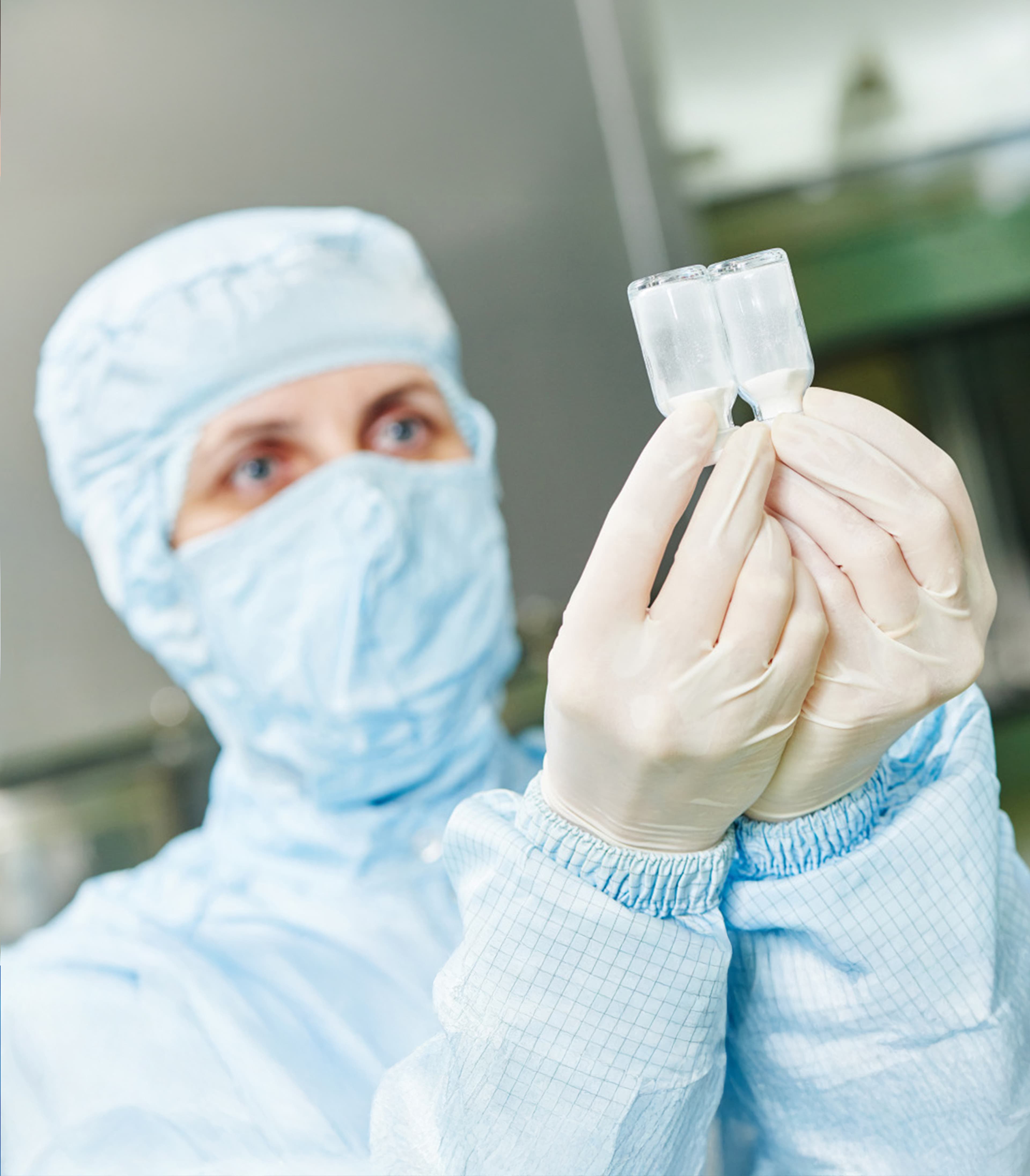 Person wearing personal protective equipment inspecting two vials