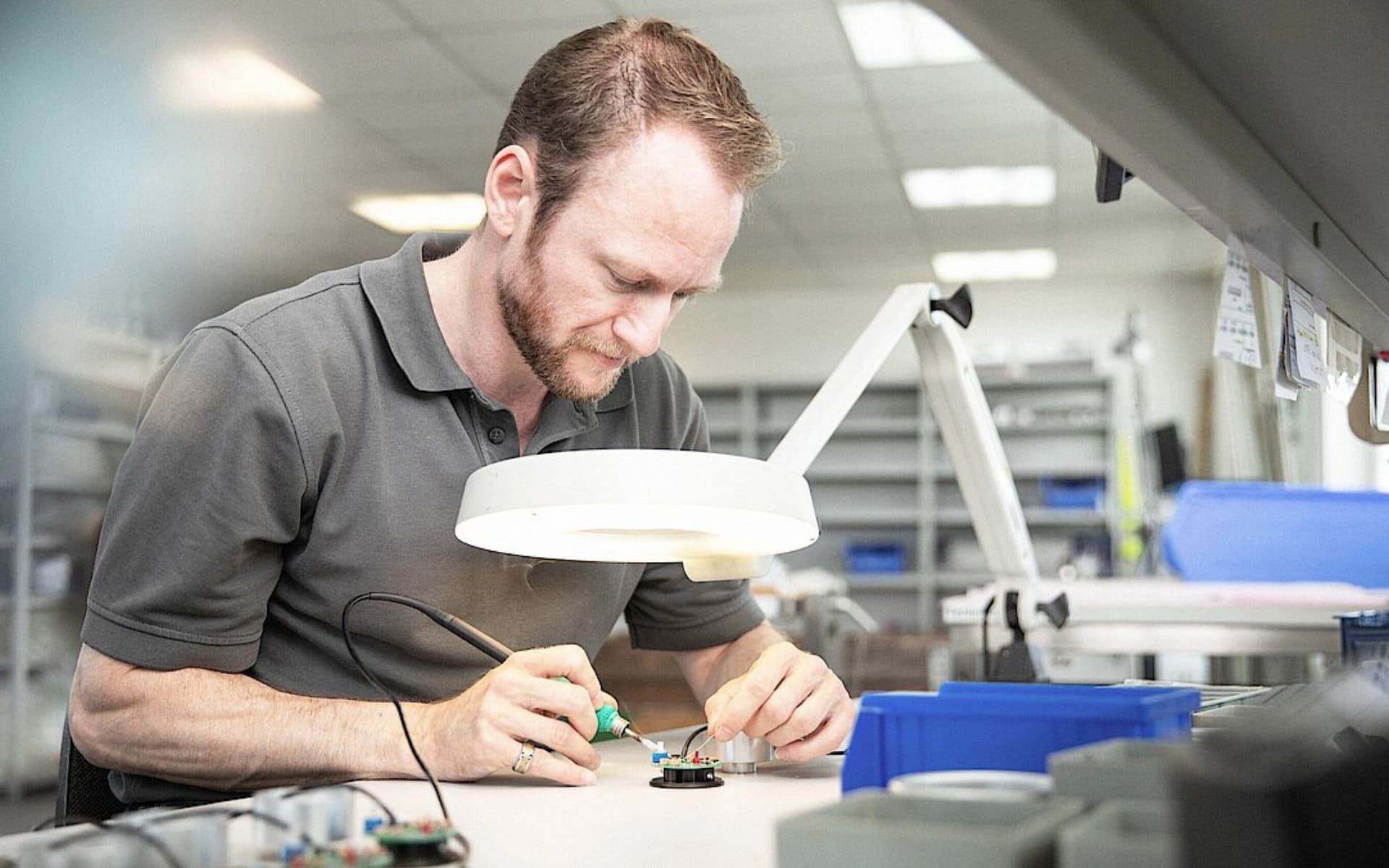 A man assembling components on a circuit board in a factory setting, focused on his work.