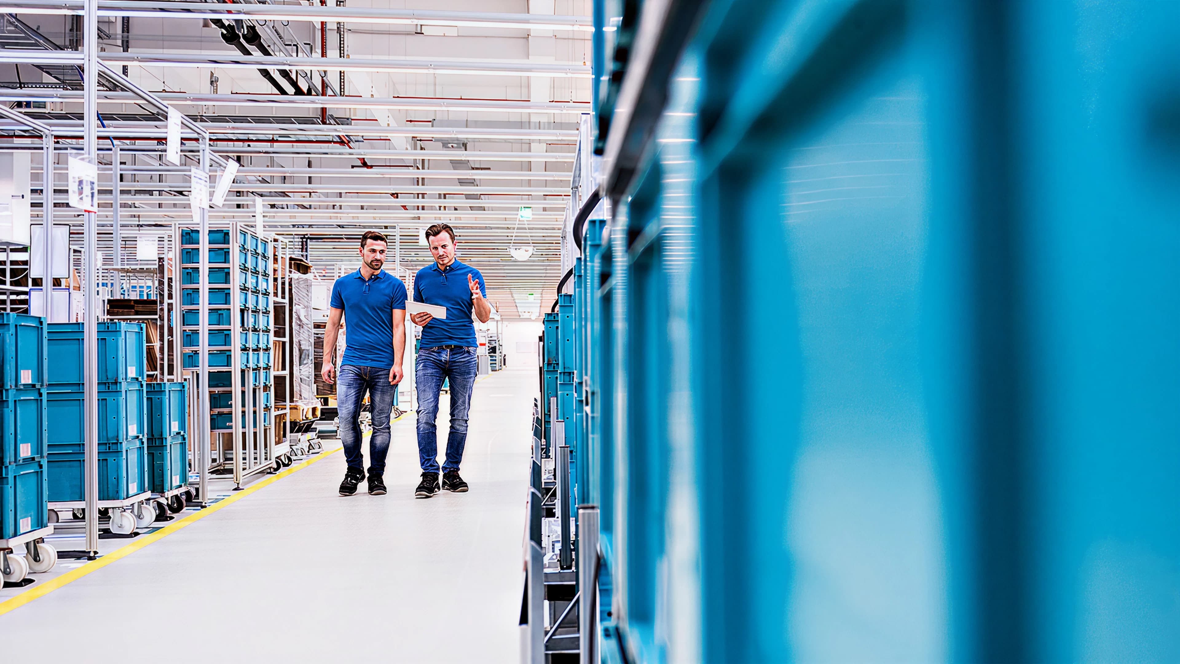 Two Körber employees walking in a warehouse with blue crates stacked in rows