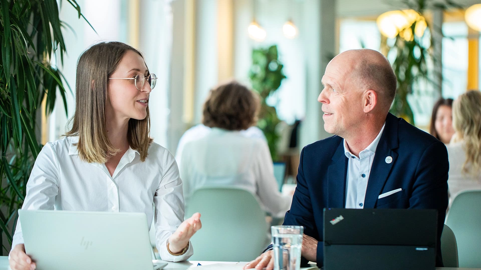Two Körber employees - a woman and a man - are sitting at a table talking to each other.