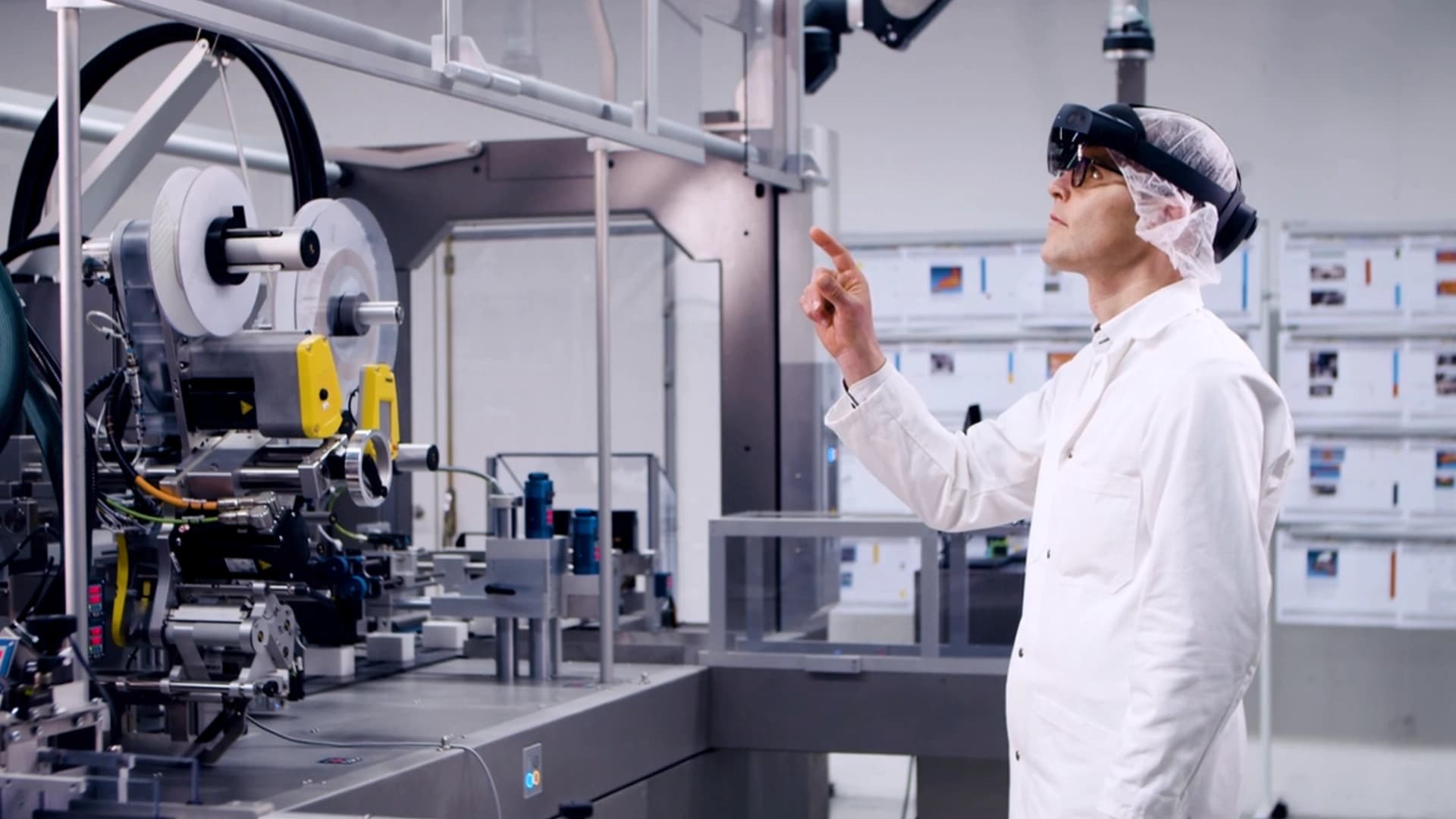 Technician in protective gear using smart glasses to operate machinery in a clean, high-tech manufacturing environment.
