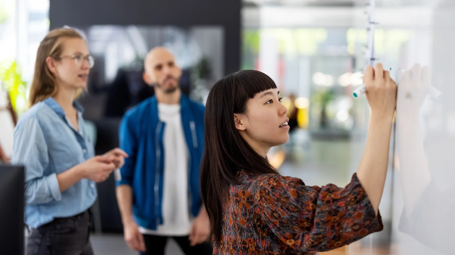 A woman is writing on a whiteboard, surrounded by a group of people who are actively participating in the session.