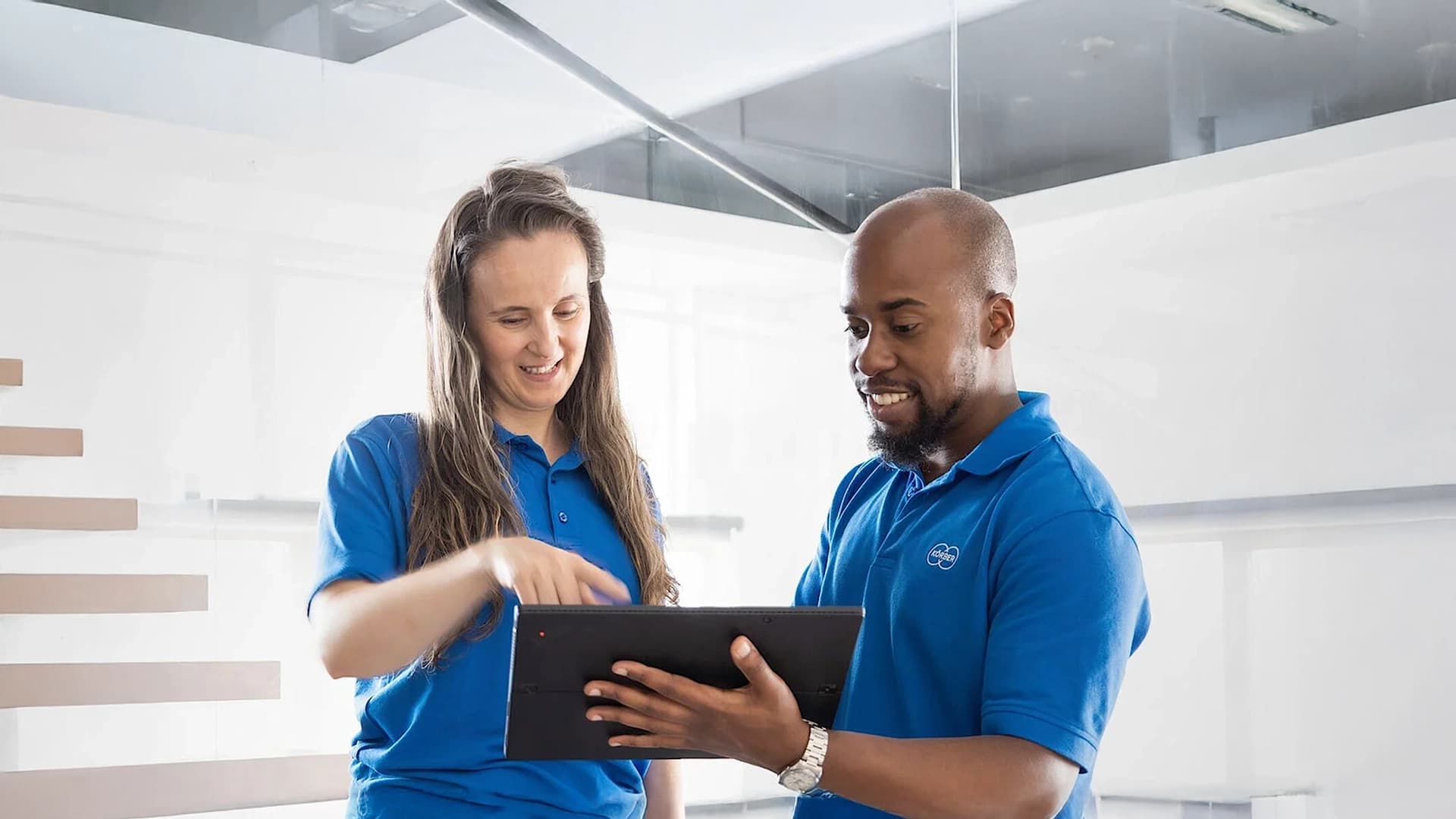 Two employees in Körber uniforms collaborating and reviewing information on a tablet.