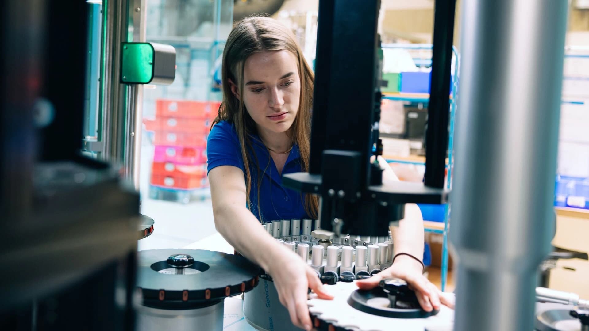 A woman works diligently on a machine in a factory, surrounded by various tools and equipment essential for production.